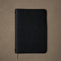 Pensift Notebook in a black Italian Epsom leather cover, seen from above on camel, beige ribbon trailing