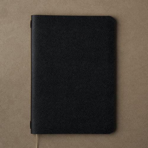 Pensift Notebook in a black Italian Epsom leather cover, seen from above on camel, beige ribbon trailing