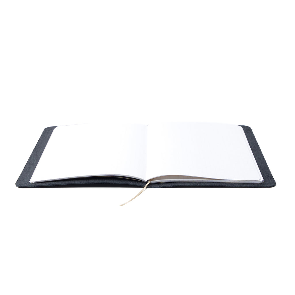 An open Pensift Notebook demonstrating its completely lay-flat design, revealing the dot grid pages and bookmark ribbon.