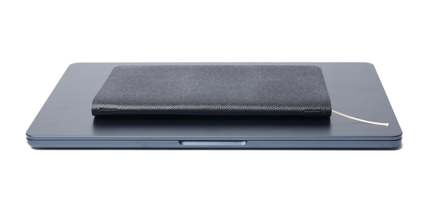 The closed Pensift Notebook resting on top of a dark grey laptop, demonstrating its incredibly slim profile and how it seamlessly fits into a modern minimalist carry.